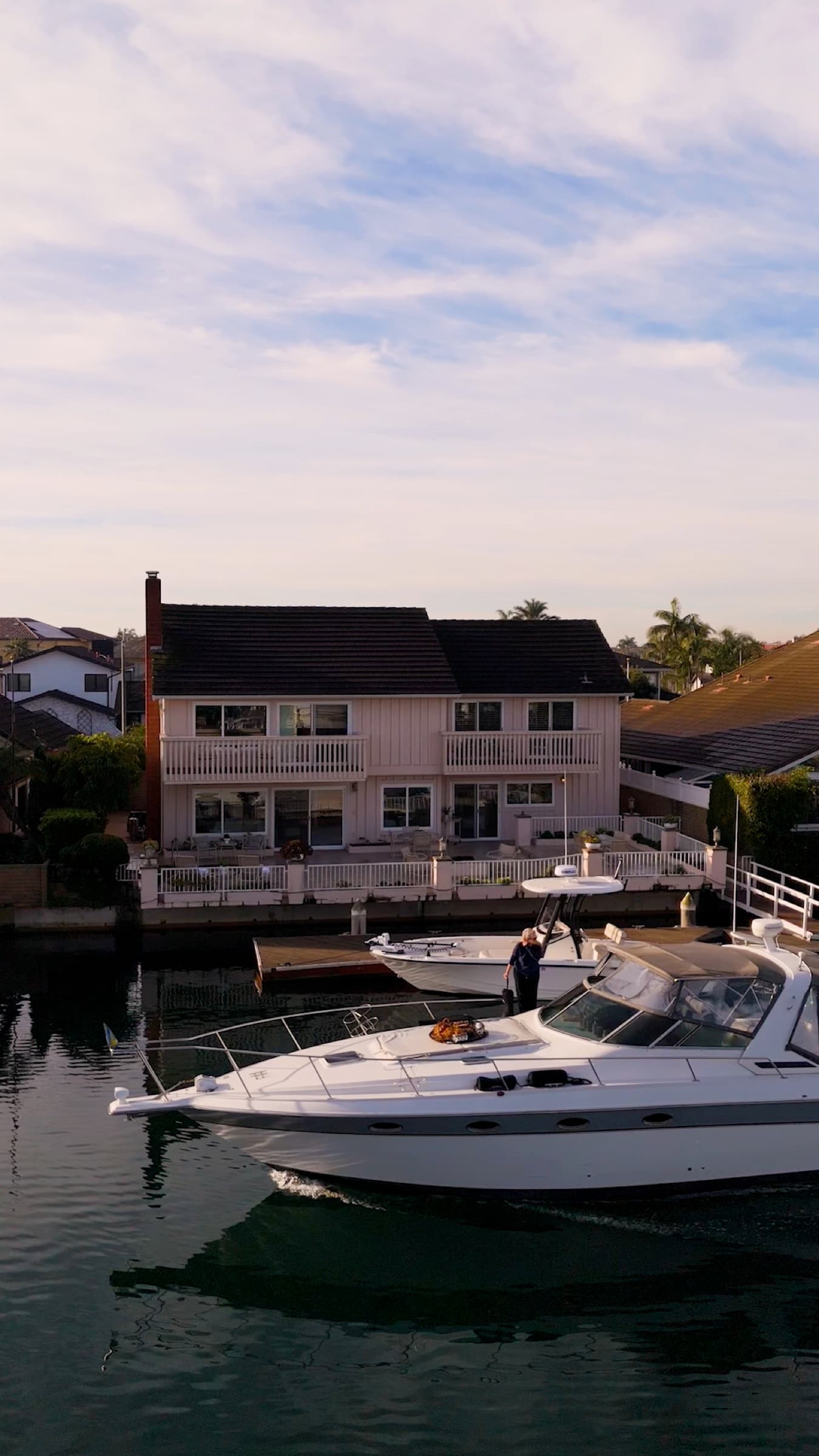 A yacht cruising the main channel of Huntington Harbour at golden hour, waterfront homes and docks along the shore.