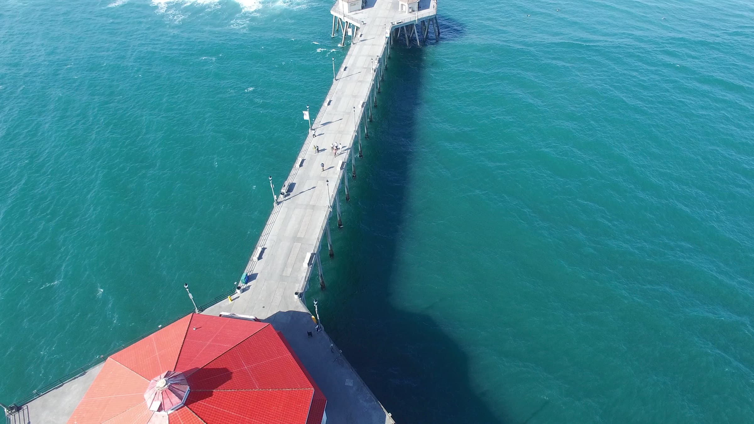 Aerial view of the Huntington Beach pier stretching over the Pacific, with the shoreline and surf below.