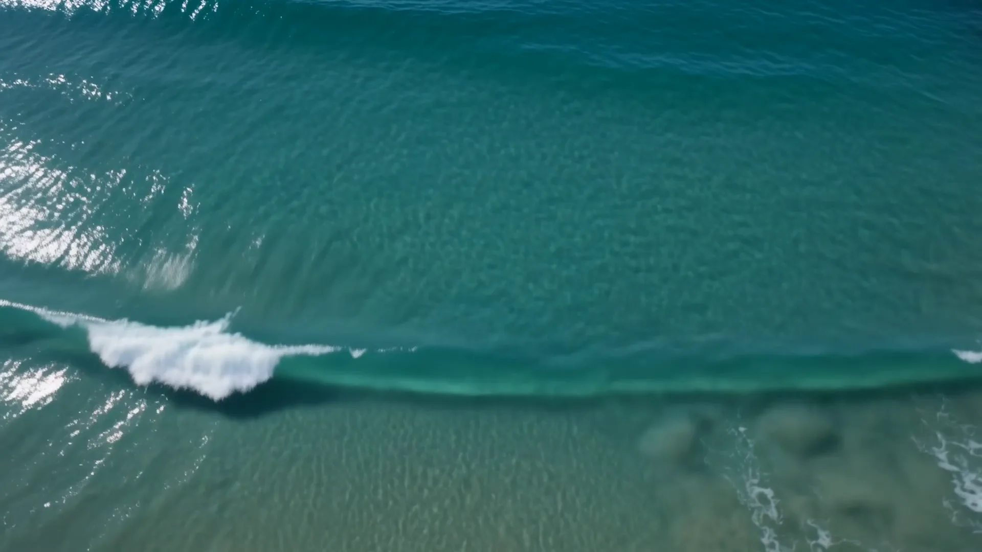 Aerial view of a breaking wave over the clear Pacific off the Huntington Beach coast.